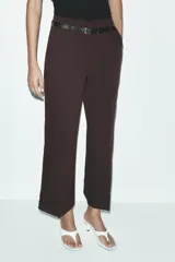 Pantalón marrón de tiro alto con cinturón negro, bolsillos delanteros y cierre frontal con cremallera y gancho metálico.
