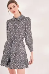 Vestido corto con estampado floral en blanco y negro, cuello camisero, mangas largas abullonadas y falda acampanada. Incluye lazo del mismo tejido para ajustar en la cintura y detalle de borlas en el ruedo.
