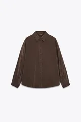 Camisa marrón de corte holgado, con cuello de solapa, manga larga con pliegues y bajo asimétrico. Cierre frontal con botones.