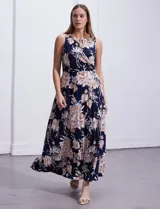 Vestido largo de seda fría con estampado floral en tonos beige y blanco sobre fondo azul marino. Tiene cuello redondo cruzado con abertura y aplique metálico.