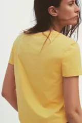Camiseta amarilla de algodón con cuello redondo, manga corta y estampado marrón con el texto "New York Fluxus 1970".
