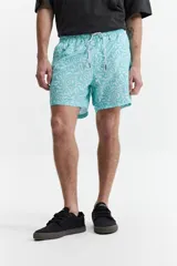 Short de baño celeste con estampado de hojas blancas, cintura elástica con cordón ajustable, dos bolsillos laterales y un bolsillo trasero.