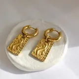 Par de aros dorados tipo huggies de acero quirúrgico hipoalergénico con baño en oro 18k y dije rectangular con diseño abstracto.