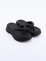 Sandalia tipo ojota o chancleta de goma negra, con plataforma gruesa y suela con textura acanalada o estriada.