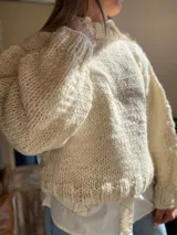 Sweater tejido de lana merino color crudo, con cuello alto y mangas largas abullonadas. Tejido artesanal con punto grueso.