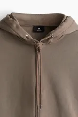 Campera con capucha color marrón topo, corte oversized, con cierre frontal, bolsillos tipo canguro, puños y bajo acanalados.
