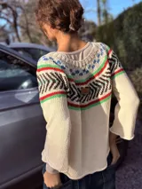 Sweater tejido a mano en hilo de algodón color crudo, con cuello redondo y mangas largas. Presenta un diseño geométrico en el canesú con detalles en azul, rojo, verde y marrón.