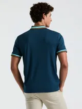 Chomba azul petróleo de manga corta con cuello polo y puños acanalados a rayas en celeste, naranja y blanco. Logo bordado en el pecho. Cierre con dos botones.