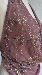 Top halter color marrón con escote pronunciado y detalle de frunce en el centro. La prenda está adornada con lentejuelas y cuentas bordadas en tonos cobrizos y rosados.