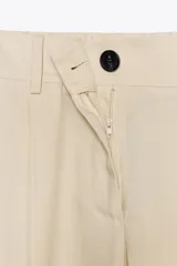 Pantalón color crema de tiro alto con pinzas delanteras y cintura elástica en la espalda. Tiene bolsillos delanteros y traseros.