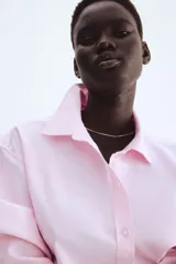 Camisa rosa de algodón Oxford con cuello clásico, botones al frente, canesú con trabilla en la espalda, corte relajado, hombros caídos, mangas largas con puños sencillos, bolsillos superiores con solapa y bajo redondeado con espalda más larga.