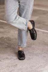 Mocasín de cuero negro con cordones y tachas metálicas en la puntera.