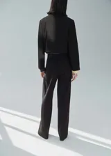 Pantalón negro de vestir, de corte recto y largo, con tiro medio, trabillas, bolsillos laterales y cierre frontal oculto con botón, gancho y cremallera. Incluye lazo ajustable en la cintura y forro interior.