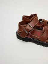 Sandalias romanas color verde oliva, con tiras entrecruzadas y hebilla lateral. Suela de goma negra con plataforma de 3cm. Fabricadas en cuero vacuno.