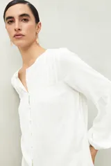 Camisa blanca de corte relajado con botones forrados a tono, canesú con pequeñas tablas y mangas amplias con puño elastizado.