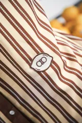 Vestido corto color crema con rayas verticales marrones, cuello mao, botones a tono y parche con logo en el frente.