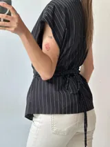 Chaleco negro con rayas verticales blancas, escote en V, corte ajustado y cierre cruzado con un botón. Sin mangas.