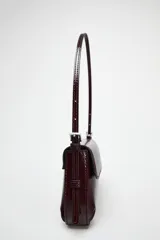Bolso de hombro color borgoña con efecto acharolado, solapa con cierre magnético y asa ajustable.