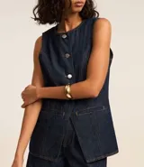 Chaleco femenino confeccionado en jeans, sin mangas, cinturado, con botones y bolsillos. De corte alargado y cuello redondo.