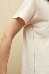 Remera de manga corta color gris claro, confeccionada en algodón con textura liviana y suave al tacto. Presenta costuras decorativas en los laterales y mangas con pequeño doblez.