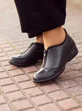 Zapato bajo de cuero negro con cierre de cremallera frontal.