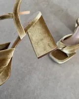 Sandalia de cuero vacuno color dorado, con plataforma y taco cuadrado. Presenta una tira delgada en el tobillo y detalle de nudo en la capellada.