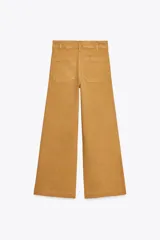 Pantalón de jean de tiro alto color negro con pierna ancha, bolsillos delanteros y traseros, y cierre frontal con cremallera y botón metálico.