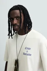 Camiseta blanca de corte holgado con cuello redondo y mangas cortas. Estampa en el pecho con la frase "Create a Narrative" en azul.