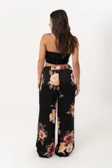 Pantalón palazzo negro con estampado floral en tonos rosa, naranja y amarillo. Tiene cintura alta con elástico.