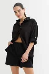 Camisa blanca de corte amplio, con cuello clásico, cierre frontal con botones y mangas largas con puños abotonados.