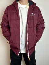 Campera inflada color bordó con capucha, cierre frontal con cremallera blanca, bolsillos laterales y logo de Santa Barbara Outfitters bordado en el pecho.