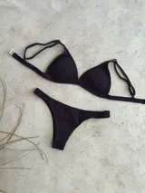 Conjunto de bikini blanco con textura, compuesto por un corpiño de triángulo fijo con breteles regulables y almohadillas desmontables, y una bombacha vedetina con frunce elástico en los costados.