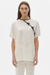 Blusa color crema tejida calada de manga corta con cuello redondo y cierre lateral con lazos negros.