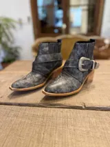 Botinetas texanas de cuero gastado color gris, con bordados blancos en la puntera y caña, hebilla decorativa plateada y taco de madera.