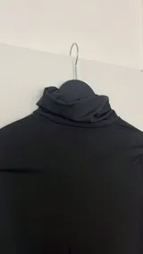 Top negro de cuello alto y manga larga, con abertura lateral en la cintura.