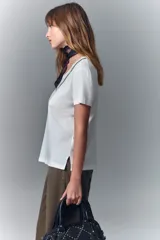 Remera blanca de algodón con cuello redondo y aplique de cadenas metálicas y strass en el escote.