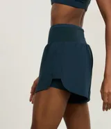 Bermuda deportiva femenina de microfibra color amarillo claro, con diseño de doble capa: un short interno ajustado y una capa externa suelta con bajo redondeado. Posee cintura alta.