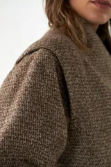 Chaqueta corta color beige, con cuello, manga larga y detalle en hombros. Forrada al tono, con bolsillos y abrochadura delantera con botones.