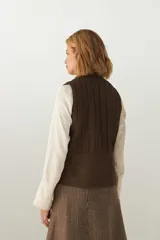 Chaleco color crema con cuello alto y cierre frontal con cremallera. Diseño con alforzas verticales en la parte superior delantera y trasera.