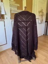 Ruana tejida a mano en color lila, confeccionada en lana merino. Presenta un diseño de punto con calados diagonales y terminación de flecos largos en el ruedo.