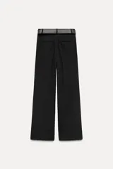 Pantalón negro de tiro alto con pinzas delanteras, pernera ancha y cinturón con hebilla dorada.