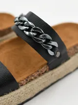 Sandalia de plataforma estilo alpargata, color negro, con dos tiras anchas sobre el empeine. La tira superior está decorada con una cadena gruesa plateada.