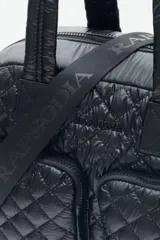 Bolso marrón con diseño matelassé, doble asa corta, correa larga desmontable y dos bolsillos frontales. Incluye llavero de corazón y dijes desmontables.