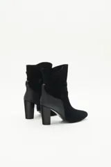 Botas de caña media de gamuza negra, con taco cuadrado y punta fina. Presenta tiras terminadas con borlas que se cruzan y atan alrededor de la caña.