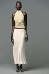 Top color crema con cuello halter, espalda descubierta, detalle de frunces y pieza metálica en forma de sol en el delantero.