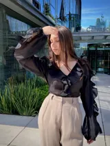 Blusa negra traslúcida con escote en V y volados en el frente y mangas largas abullonadas.