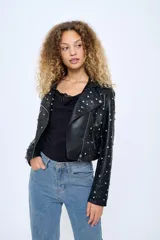 Chaqueta corta estilo motoquera de cuero sintético negro, con cuello solapa y cierre cruzado con cremallera. Decorada con tachas plateadas en solapas, hombros y mangas.