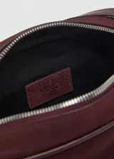 Bolso pequeño de piel bovino color borgoña, con forma rectangular y esquinas redondeadas. Cuenta con asa larga ajustable de cuero liso y cierre de cremallera.