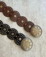 Cinto marrón de cuero sintético con apliques metálicos dorados y hebilla circular grande.