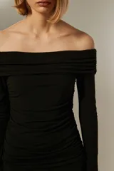 Vestido negro corto con escote off-shoulder, mangas largas y falda con volados. Diseño ajustado al cuerpo.